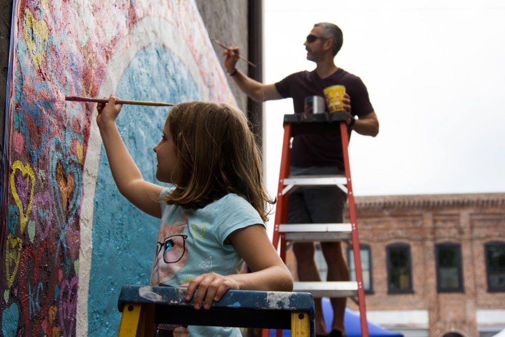 Peter Elder and his 7-year-old daughter Norah, simultaneously paint hearts onto the "Love, Graham Arts Festival" mural. This is meant to represent them giving their hearts to the Graham community, May 20.