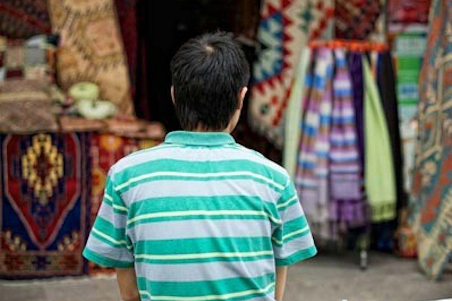 GLOBAL LOANS: A young boy waits for customers in front of his carpet stall at an outdoor bazaar in Selcuk, Turkey. Microloan organizations such as Kiva target similar individuals and small businesses to offer small-scale loans to. (Photo by Michael Arellano)
