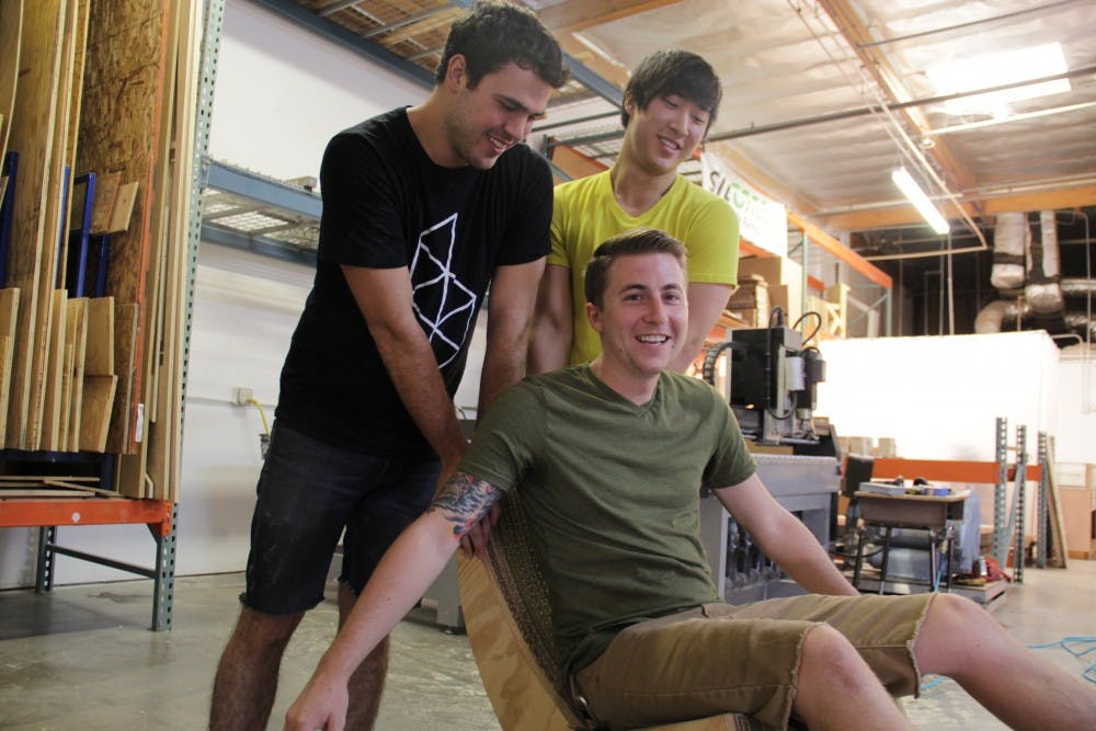 SITGREEN president and founder Jon Irons gets rocked by Jackson Minton, fabricator, and Alan Hsieh, product designer, in one of the company’s original furniture pieces.This piece was made with recycled cardboard. (Photo by Shawn Raymundo)