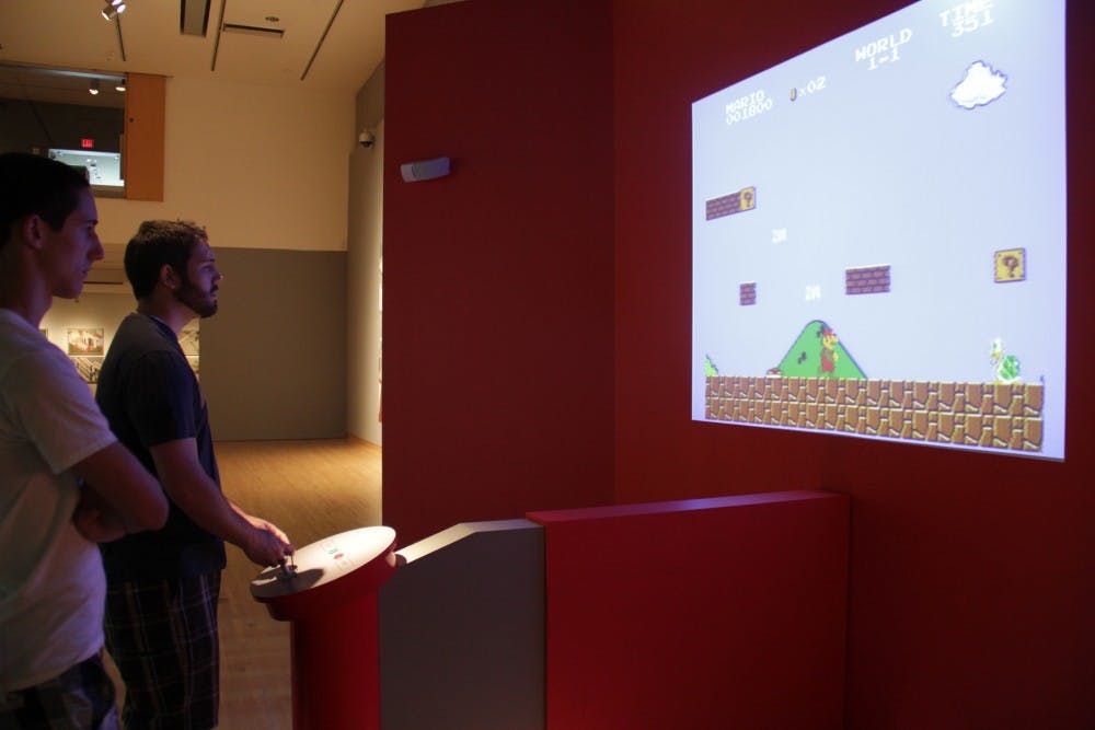Lucas Corbitt, 16, watches his brother and biochemistry sophomore Michael Corbitt play Super Mario Bros. at the Art of Video Games exhibit at the Phoenix Art Museum Saturday afternoon. (photo by Shawn Raymundo)