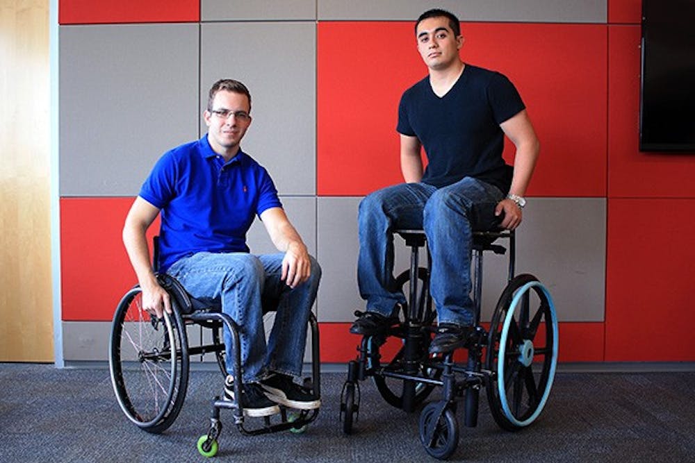 Supply chain management alumnus Peter Georgiou (left) on a conventional wheel chair and Bio-medical engineering graduate student Chris Miranda on the elevated wheel chair illustrate the difference in heights that can be achieved through this innovation. This chair allows the user to increase the elevation by ten inches. (Photo by 