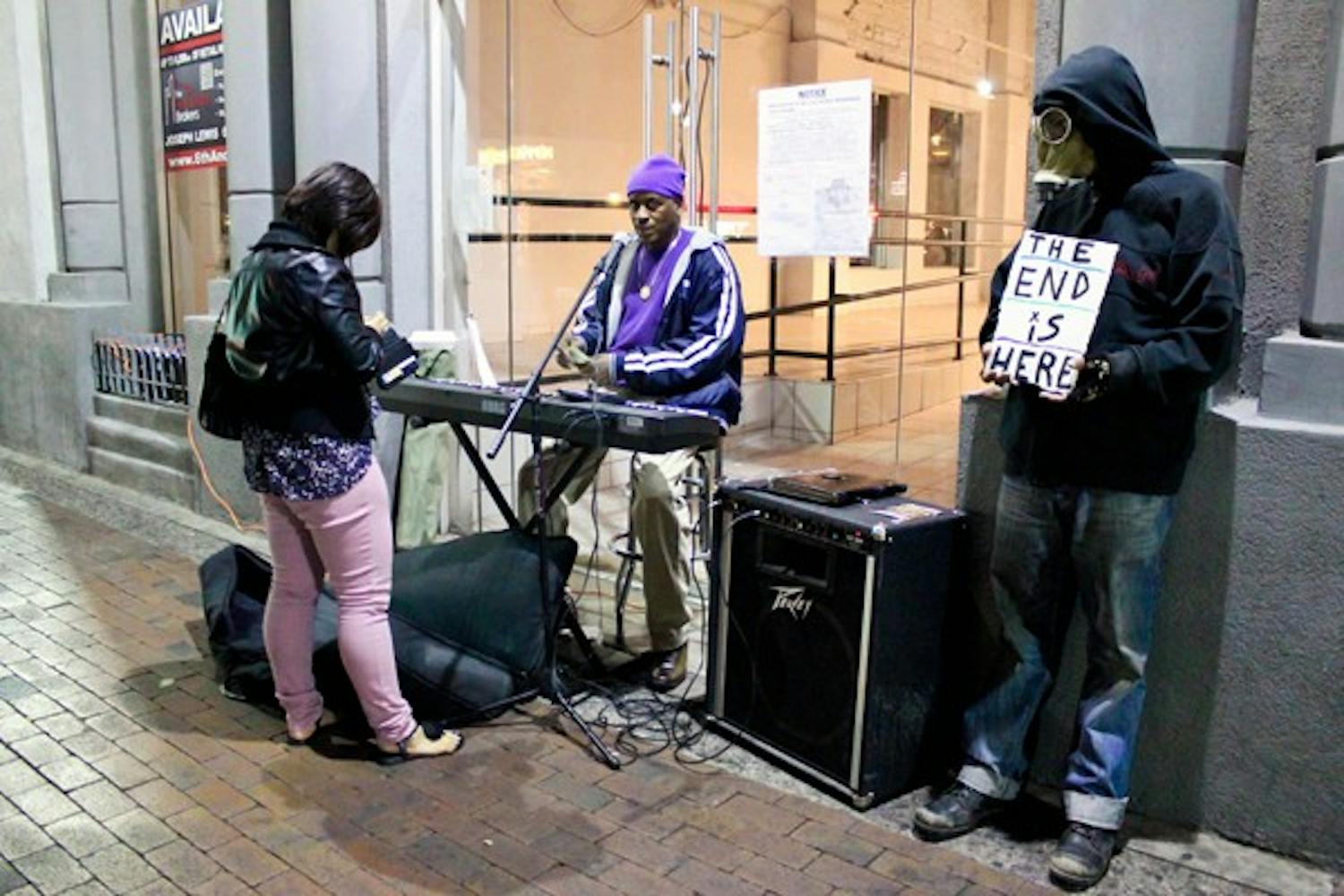 A man in purple, who refused to disclose his name, performs on Mill Avenue for extra cash while a homeless man named Sideshow wearing a gas mask holds a sign informing bystanders that “The End is Here.” (Photo by Marissa Krings)