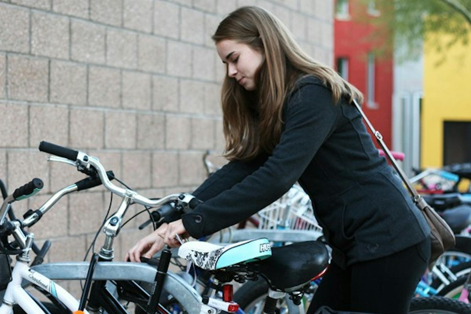 Freshman management major Raquel Thosesen locks up her bike after riding into the Barrett corridors in Tempe on Monday. Barrett Deans have threatened to ban bikes in the complex or station security guards at entrances if the Walk Your Wheels mandate is not obeyed. (Photo by Perla Farias)
