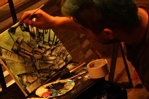 Joe Gonzalez, one of the eight visual artists at the Tempe Starving Artist Round Robin in Downtown Phoenix Friday night, knelt on the ground finishing the final details of his most recent work as the six evening bands played behind him. (Photo by Jessie Wardarski)
