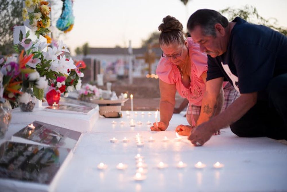 As night approaches, families lit candles at the burial sites of their loved ones. Earlinda and Joe Felix light their candles in the shapes of crosses at the graves of the deceased members of their close family.