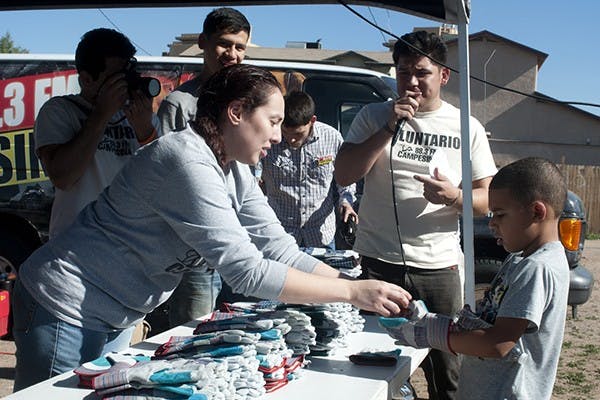 At the MLK day of service, neighborhood clean up, volunteers gather around the streets of 7th Avenue and Pima in Phoenix to hand out free work gloves to facilitate the neighborhood clean up." 

"On January 20th a handful of youths gather to share a few words as the rest of the crowd waits for further instructions. The MLK day of service neighborhood clean up aims to bring the community closer together while simultaneously improving their neighborhood. (Photo by Mario Mendez)