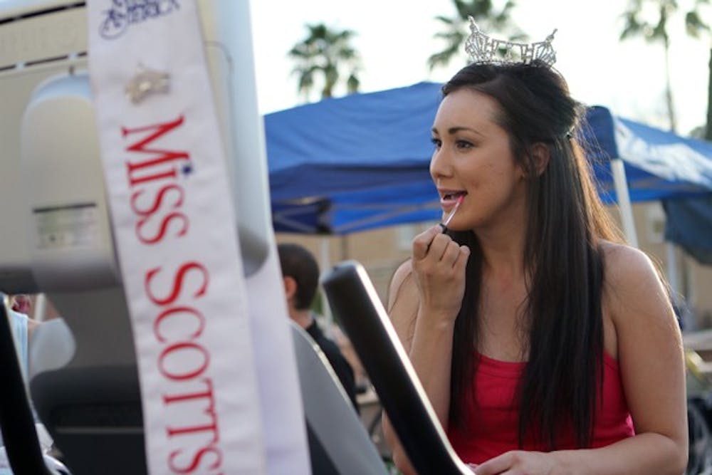 Tiffany Hilburn, Miss Scottsdale 2012, puts on lip gloss while riding a stationary bike as a participant in Pi Kappa Phi's annual Bike-A-Thon on Hayden Lawn Wednesday evening. (Photo by Lisa Bartoli)