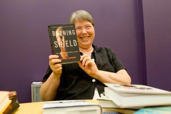 ASU Book Group member Laura Hogue holds up next month's book reading called "Burning Shield" on Sept. 2.