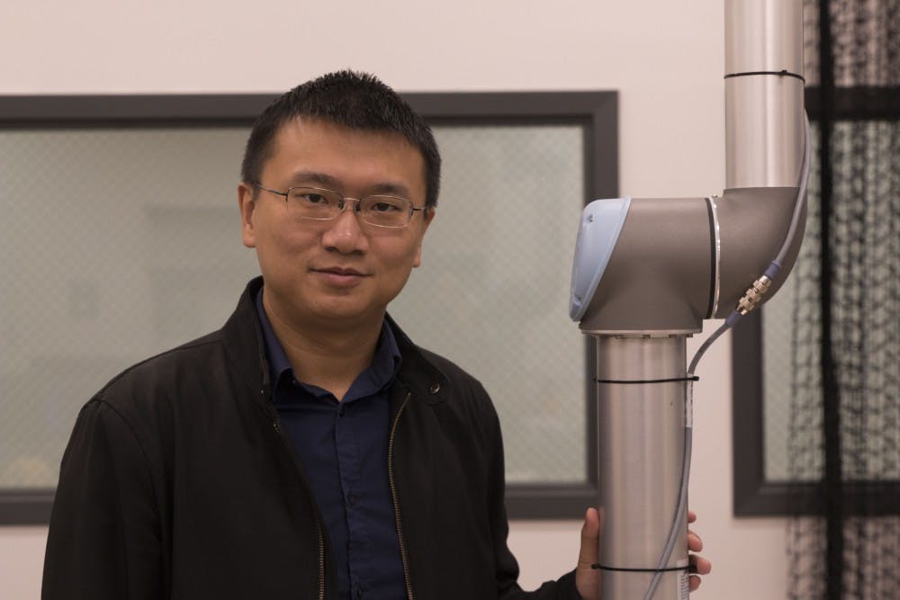 Dr. Wenlong Zhang stands in his lab&nbsp;next to a robotic limb, similar to one found in a car factory. Zhang and his team of researchers are developing ways for robots to work alongside human workers, making actions more efficient and safer for people.