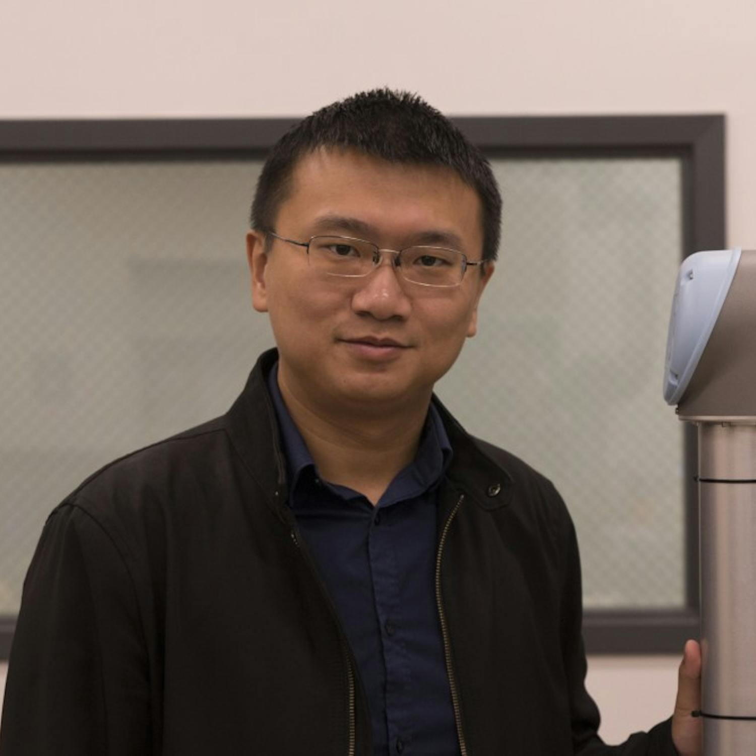 Dr. Wenlong Zhang stands in his lab&nbsp;next to a robotic limb, similar to one found in a car factory. Zhang and his team of researchers are developing ways for robots to work alongside human workers, making actions more efficient and safer for people.