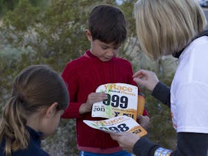 A volunteer helps pin a number on two children for the 1-mile run at Y Race Phoenix at South Mountain Park in Phoenix, Ariz., on Sunday, Oct. 20, 2013. The 45th annual Y Race Phoenix is the oldest road race in Arizona. (Photo by Caitlin Cruz)