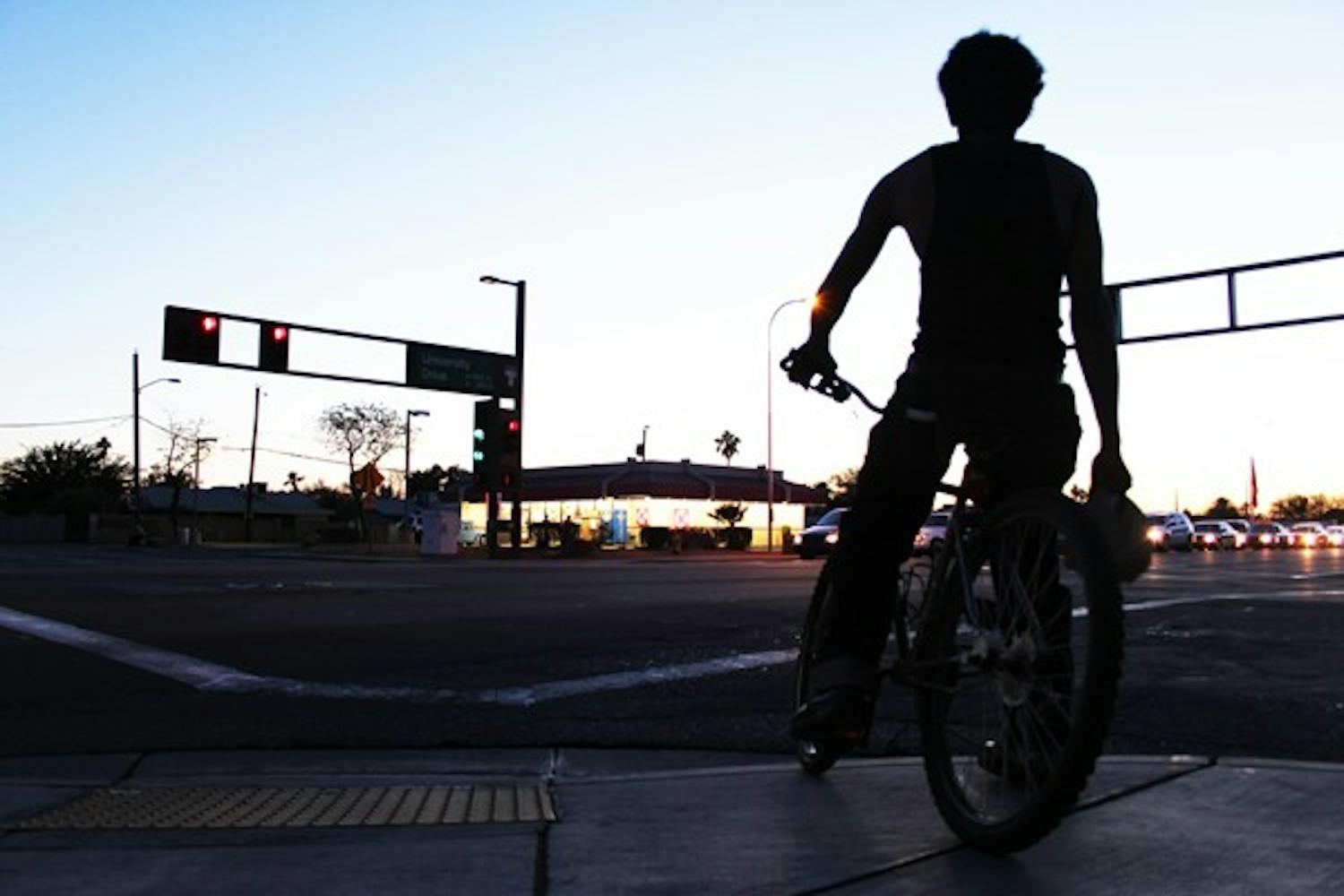 A bicyclist waits to cross the intersection of University and Hardy drives Monday night during rush hour. (Photo by Ana Ramirez)