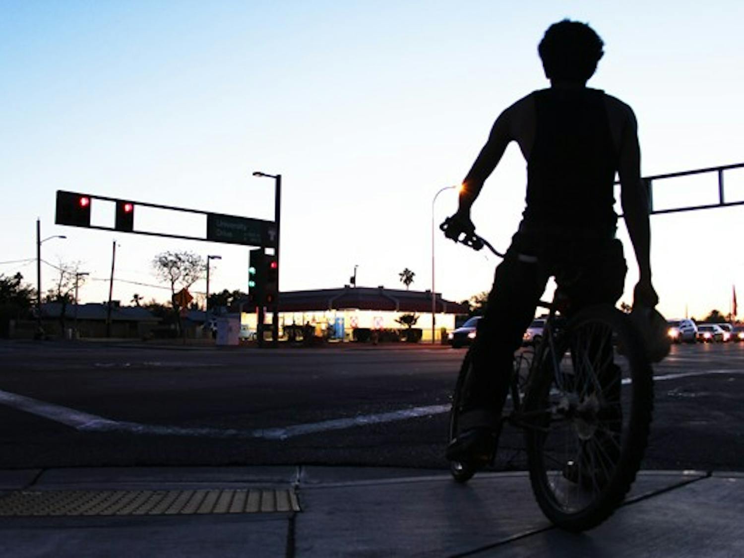 A bicyclist waits to cross the intersection of University and Hardy drives Monday night during rush hour. (Photo by Ana Ramirez)
