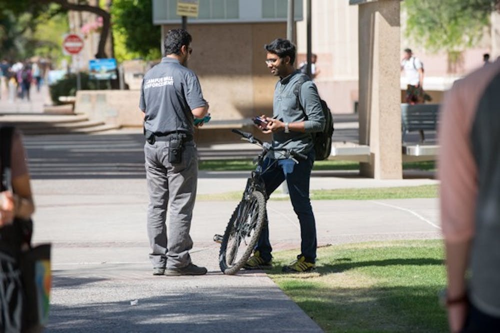 A mall enforcement officer writes in his ticket book while speaking to a stopped bicyclist. First time offenders will be given a warning while second-time offenders will be required to pay a $15 fee and attend a bicycle safety class. (Photo by Andrew Ybanez)
