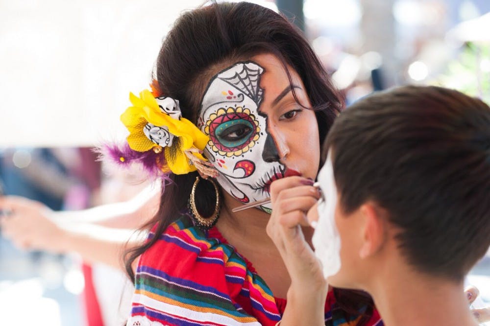A woman paints a skeleton face on a young visitor at the 2015 Dia de los Metros at the Mesa Arts Center.