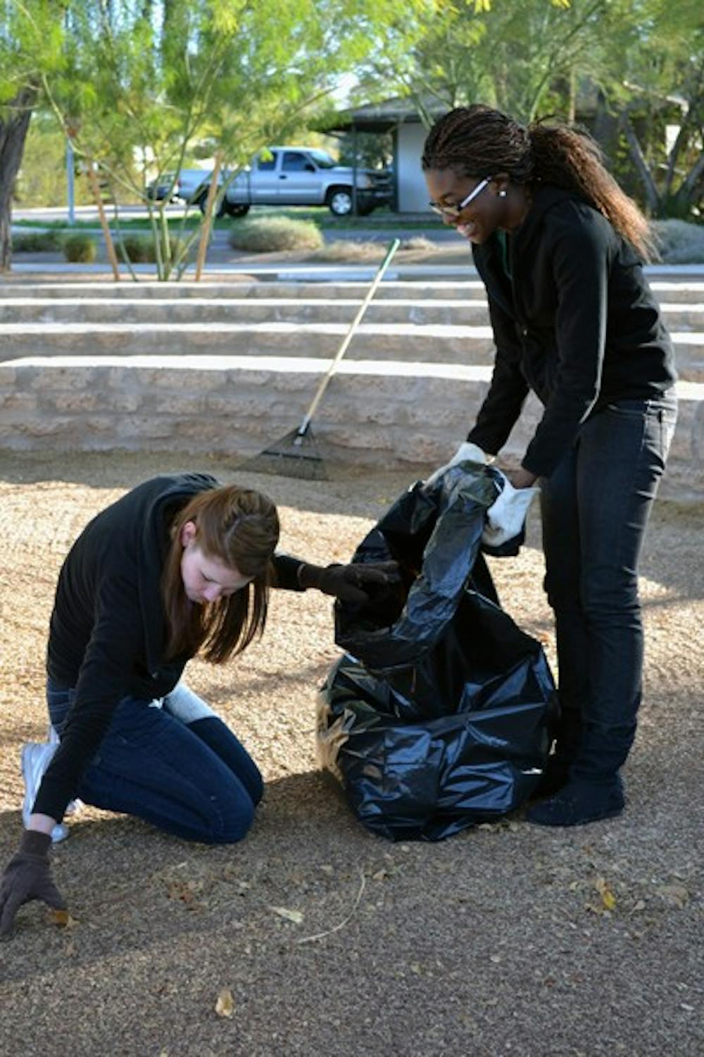 Global studies senior Dilim Dieke holds a trash bag for ASU alumna Renee Firing as they clean up leaves and twigs from Hudson Park in Tempe. Off-campus ministry group The Faithful City brought volunteers to the park Saturday morning to help clean up fallen leaves and trash.  (Photo by Mackenzie McCreary)
