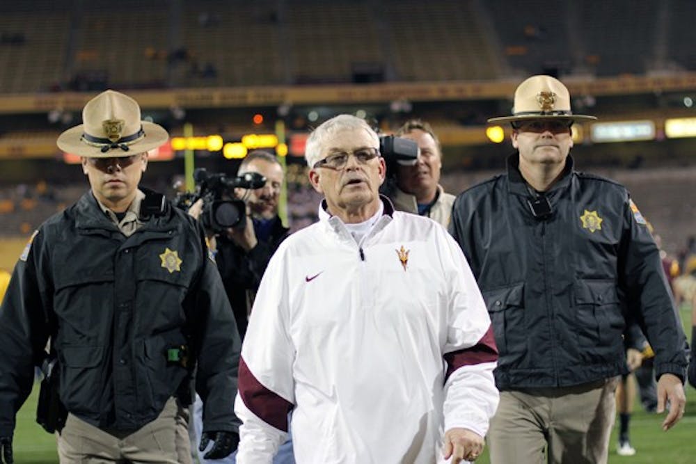 ASU coach Dennis Erickson is escorted off the field after the Sun Devils' loss to UA on Friday. Erickson was formally relieved of his duties Monday, but will coach ASU at a bowl game. (Photo by Lisa Bartoli)
