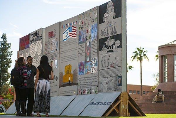 Ph.D student Zohair Zaidi talks with Global Studies major, Alicia Nelson, about the Palestinian apartheid wall constructed on Hayden Lawn. Zohair is the cofounder of Students for Justice in Palestinian at ASU, who constructed the wall to raise awareness about the issues in Palestine. (Photo by Murphy Bannerman)