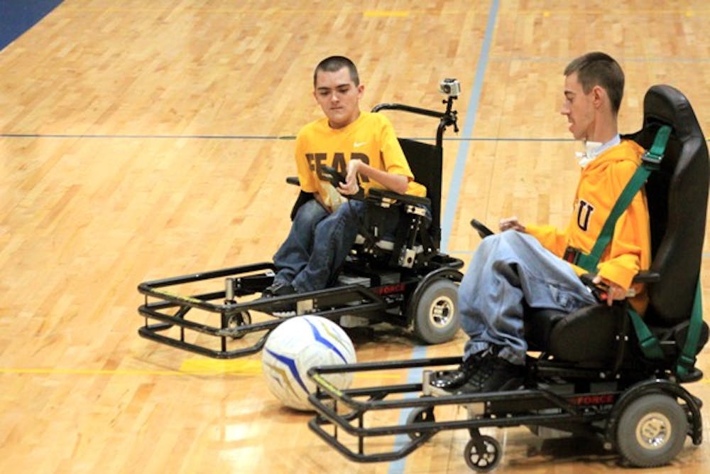 Jordan Dickey (left) and Joey Wells (right) compete for possession of the ball at a practice for the ASU Power Soccer team. Players use the guards on the front of their power chairs to maneuver a large soccer ball around a basketball court. (Photo by Ashley Kesweder)