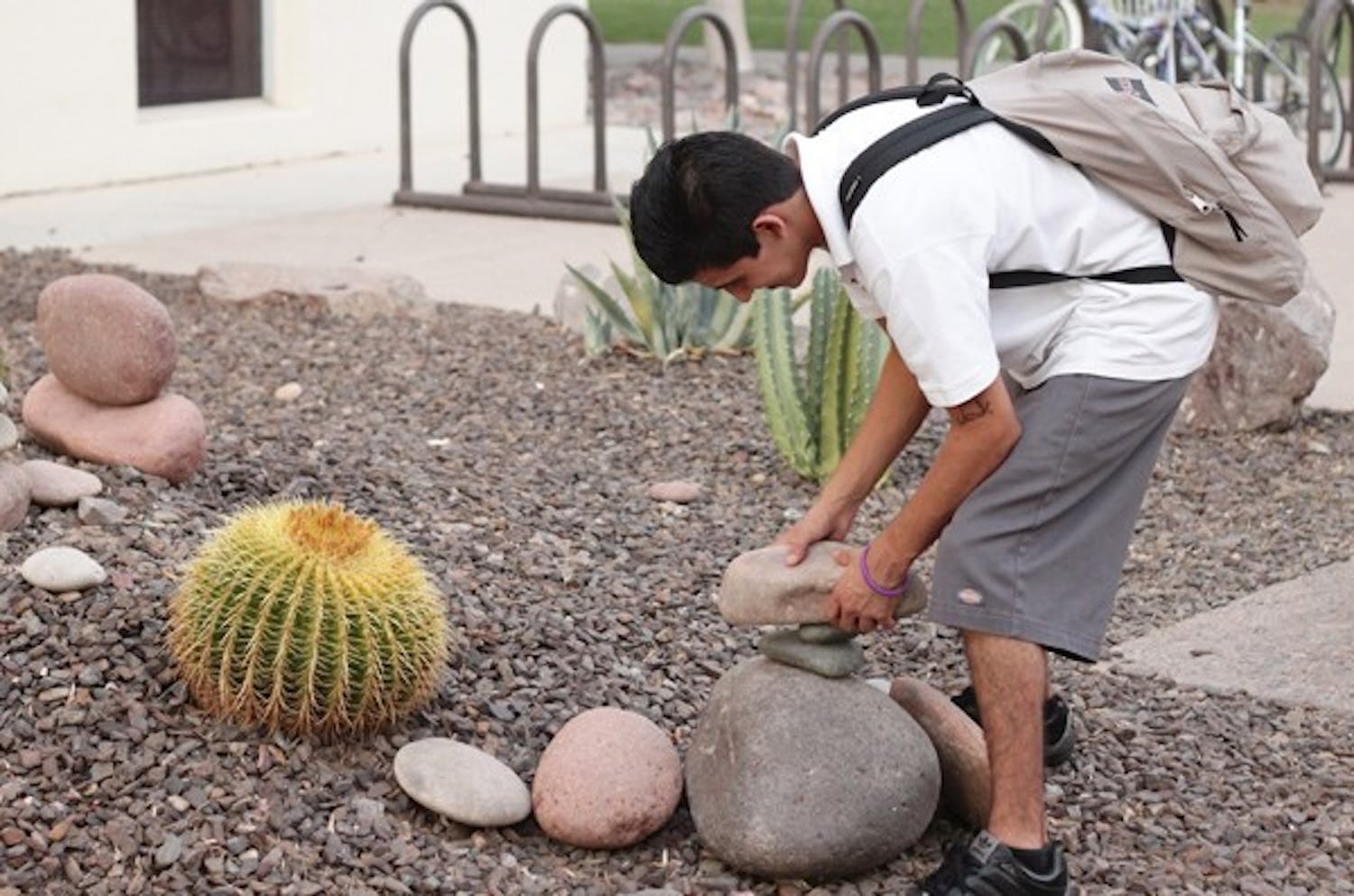 BALANCING ACT: Matthew Bracamonte, an Elementary Education junior, attempts to balance rocks outside the Matthews Center on the Tempe campus. Bracamonte said last year he used to knock the rocks down and so this semester he decided he would try to stack them up. (Photo by Beth Easterbrook)