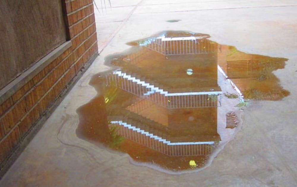 H.B. Farmer Education Building is reflected in a puddle left by excess plant water on Thursday afternoon. (Photo by Robin Kiyutelluk)