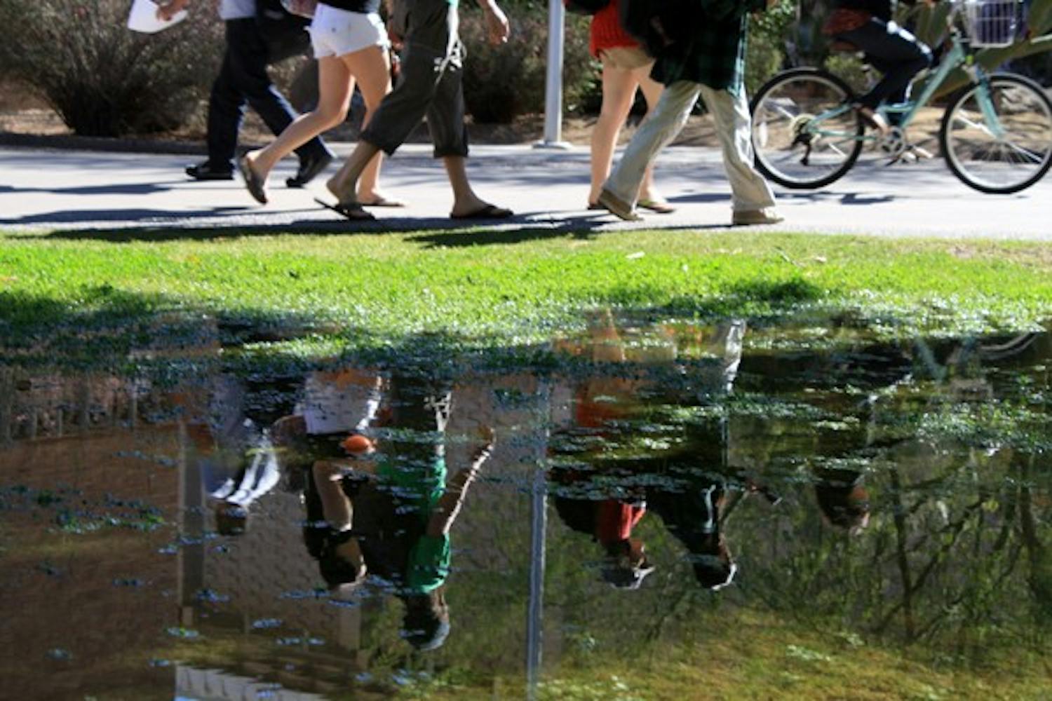 A puddle in the grass along Hayden Mall creates reflections of students walking and riding to class on the Tempe campus Monday afternoon. (Photo by Jessie Wardarski)