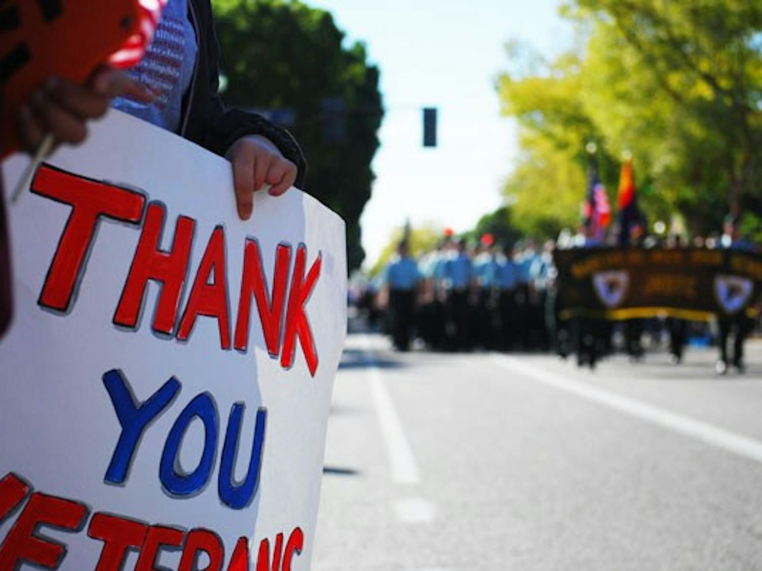 A spectator holds a "Thank you Veterans" sign as the junior RTC of Marcos De Niza High School marches down Mill Avenue during the Tempe Veterans Day parade, Monday morning. (Photo by Murphy Bannerman)