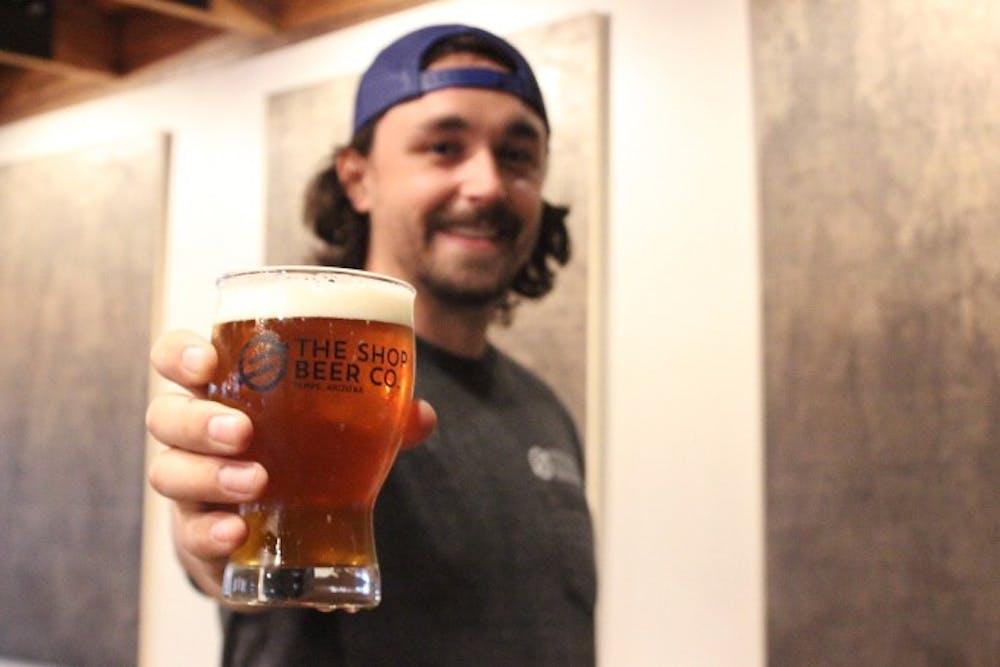 Dylan DeMiguel holds up a pint of beer behind the bar of The Shop Beer Co. 