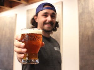 Dylan DeMiguel holds up a pint of beer behind the bar of The Shop Beer Co. 