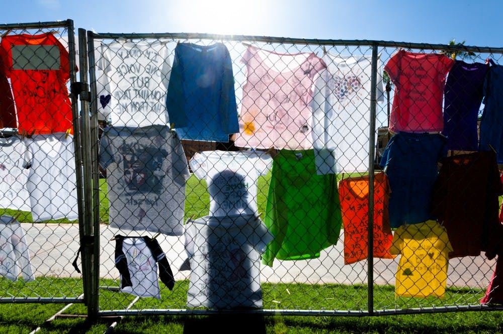 A pedestrian walks past a display of t-shirts put up by the Clothesline Project on Tuesday, Oct. 28, 2014, on Hayden Lawn in Tempe. The project sought to bring awareness to and end the stigma surrounding gender-based violence.