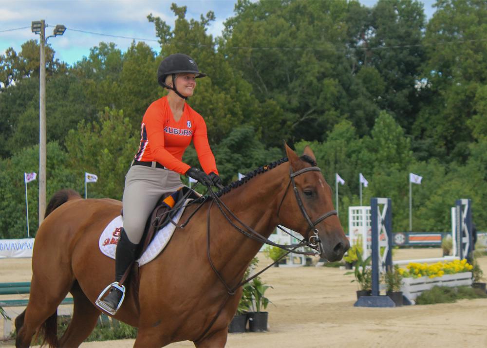 Auburn equestrian rider in a navy shirt and black cowboy hat competes on horseback inside the Auburn University Equestrian Center.