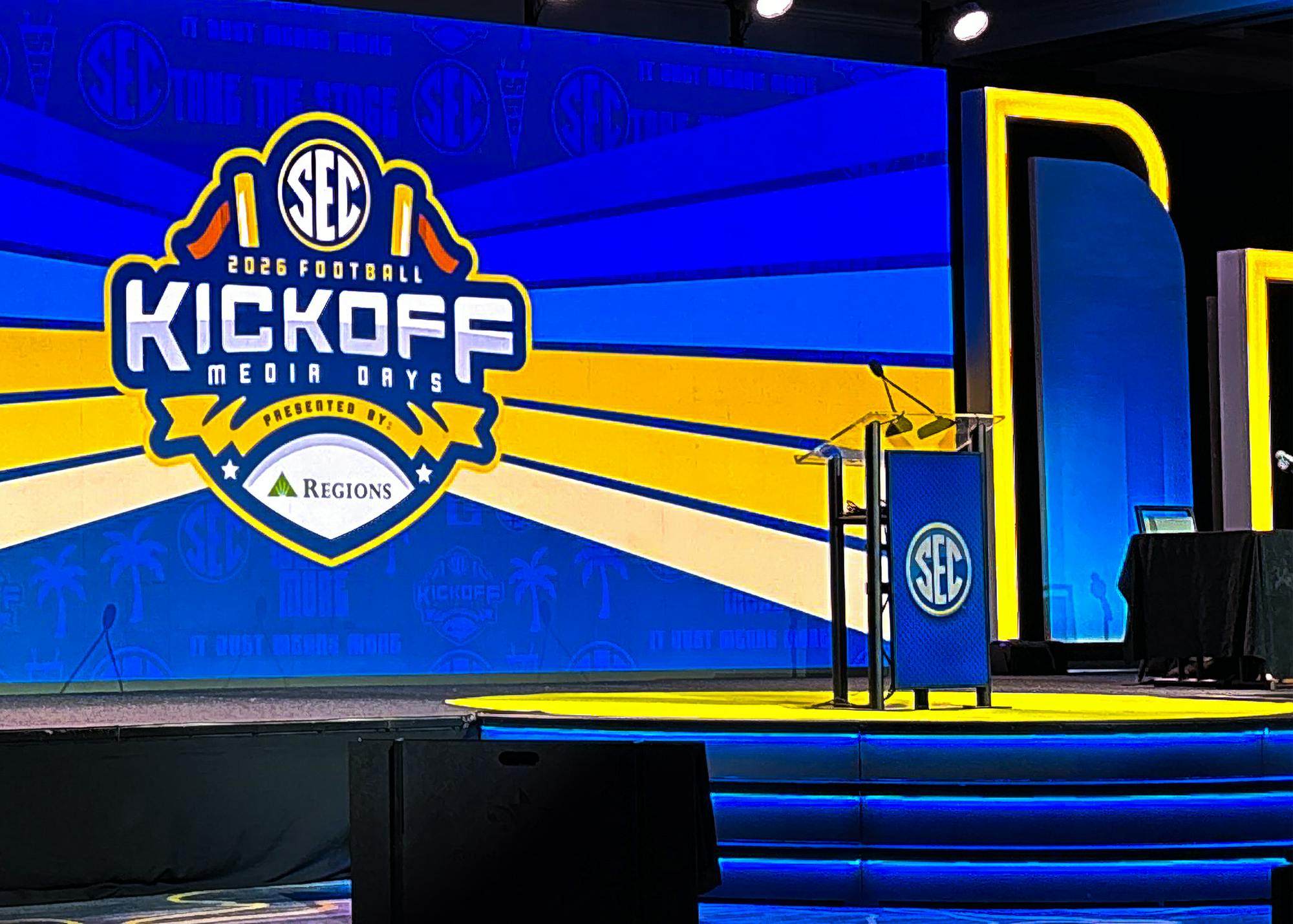 An empty SEC-branded podium stands on the stage at 2026 SEC Football Kickoff Media Days in front of a large screen displaying the event logo.