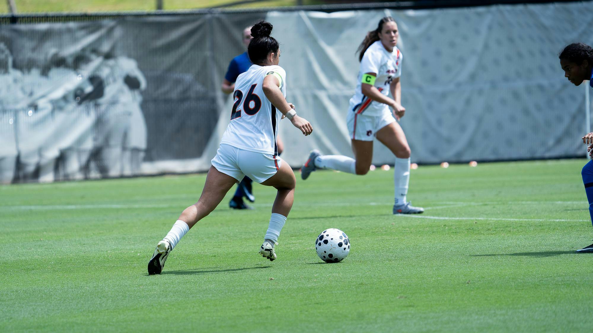 Auburn soccer player Erin Flurey, wearing jersey No. 26 in white, dribbles the ball upfield during a match, with a teammate and an opponent in pursuit.