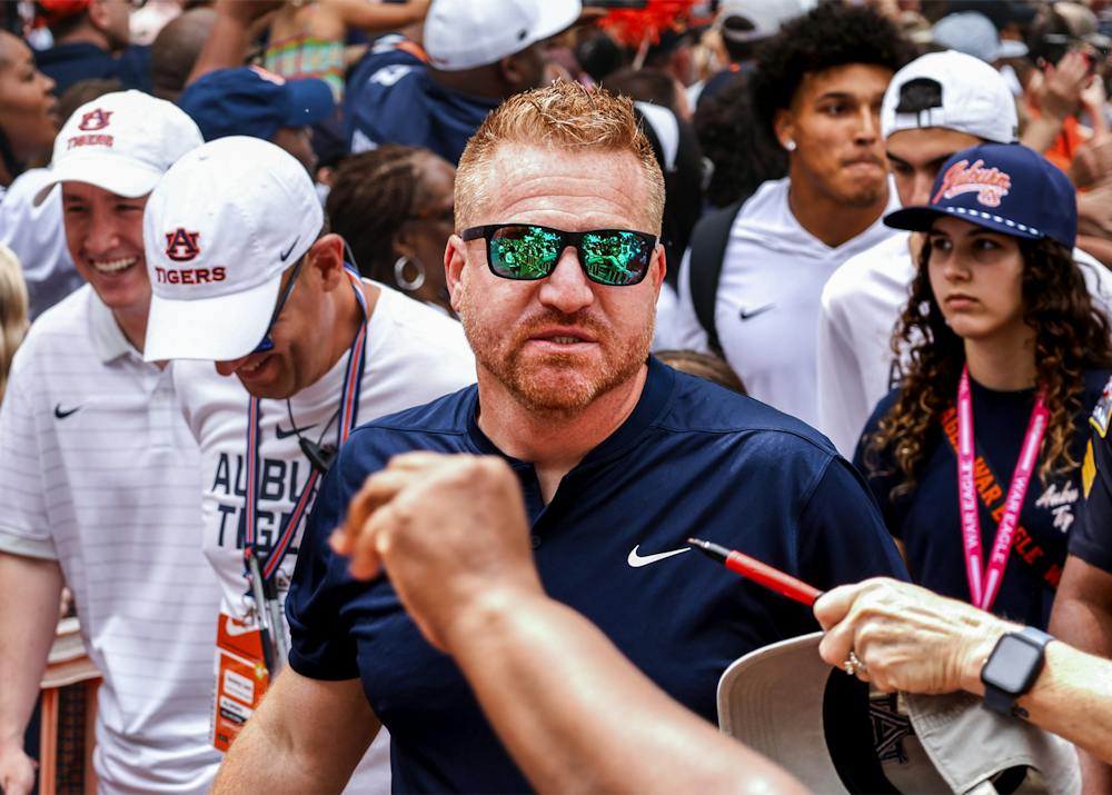 Auburn head coach Alex Golesh walks through a crowd of fans wearing sunglasses and a navy Auburn shirt during a game day.