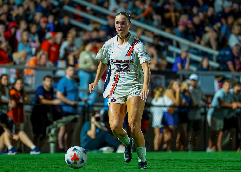 Auburn soccer player No. 32 runs toward the ball during a match, with fans seated in the stands behind her.