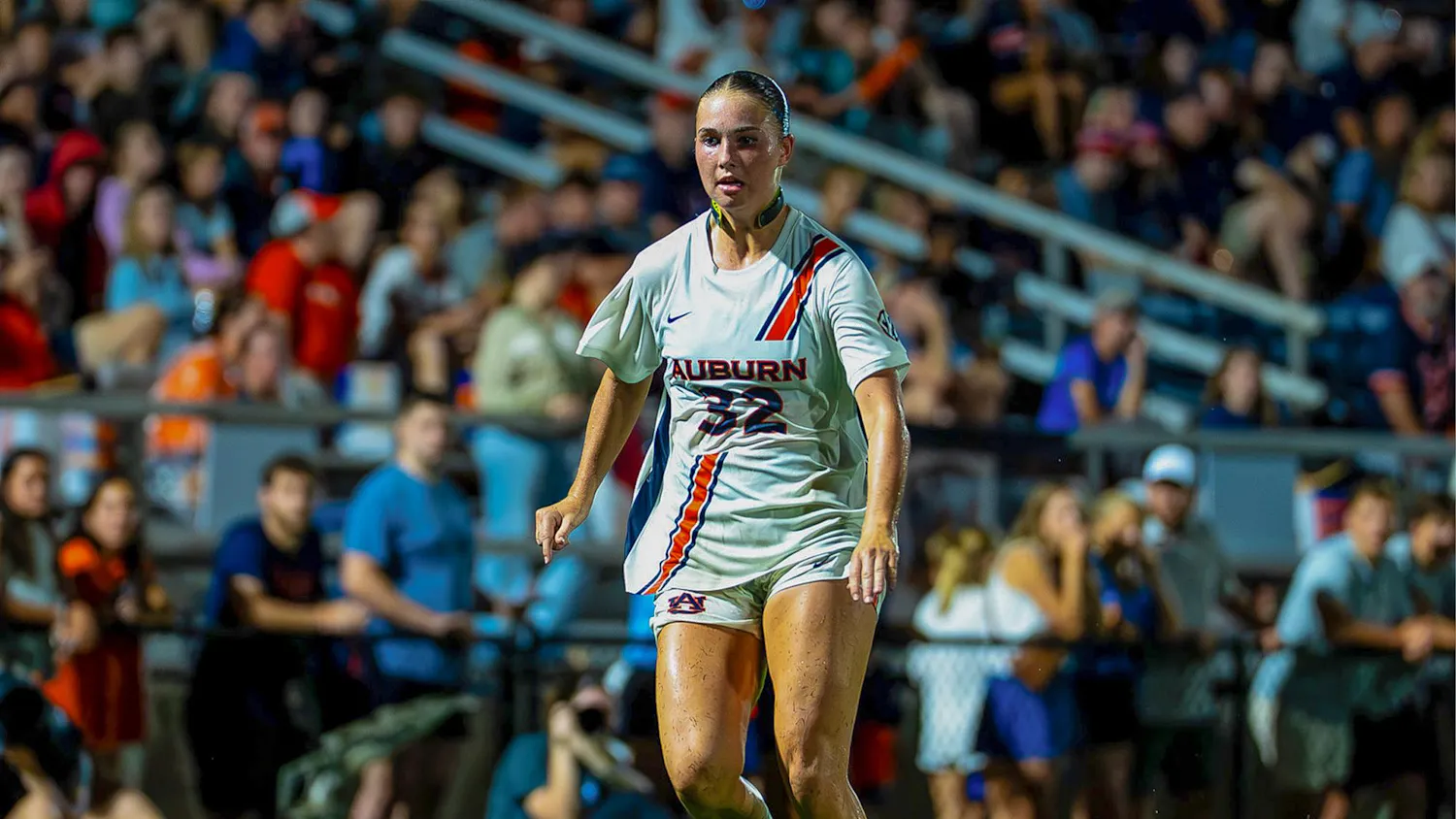 Auburn soccer player No. 32 runs toward the ball during a match, with fans seated in the stands behind her.