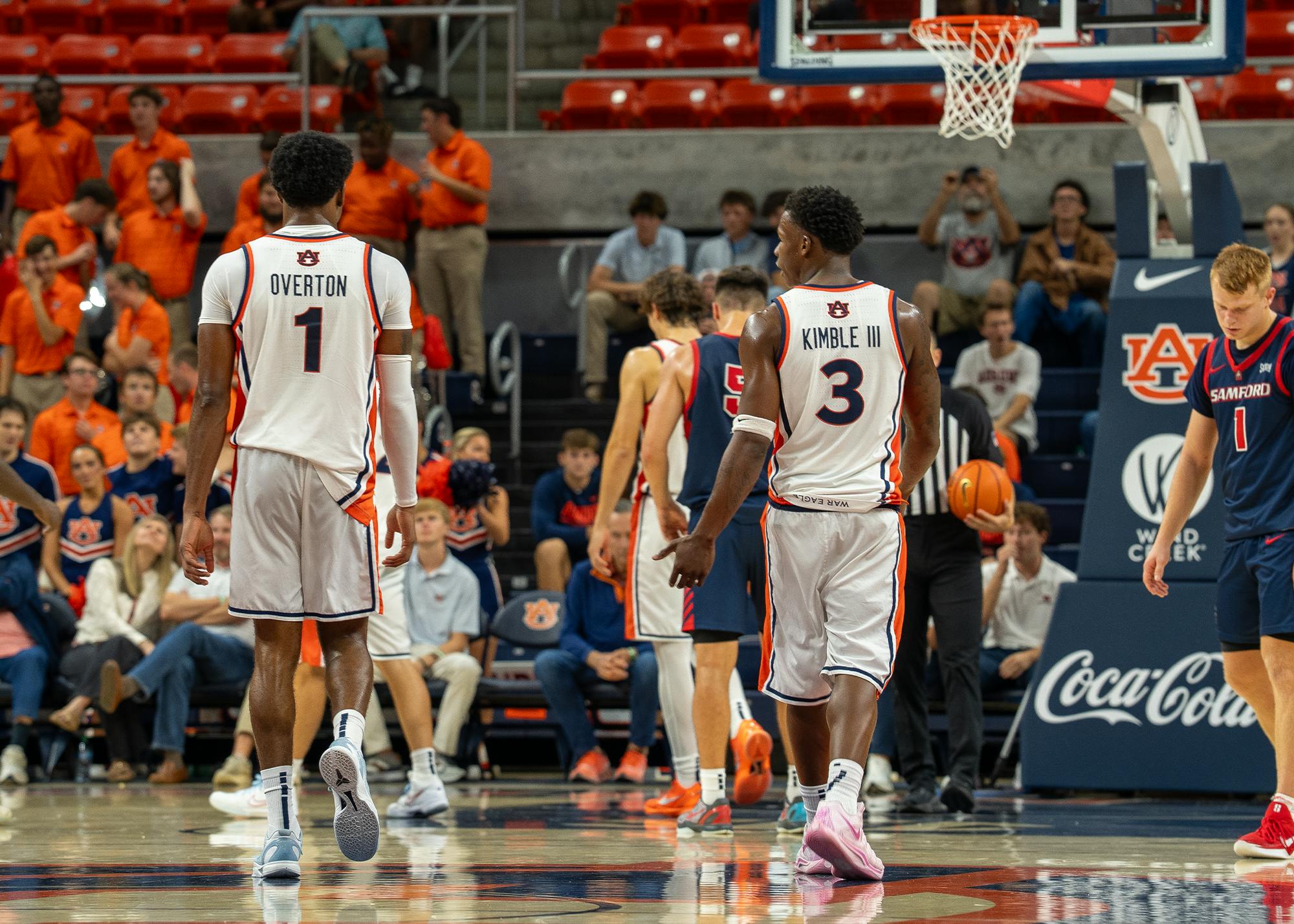Auburn Men's Basketball players Miles Kelly (#1, labeled Overton on back) and JP Pegues (#3, labeled Kimble III on back) walk back down the court in white uniforms during a college basketball game against Samford.