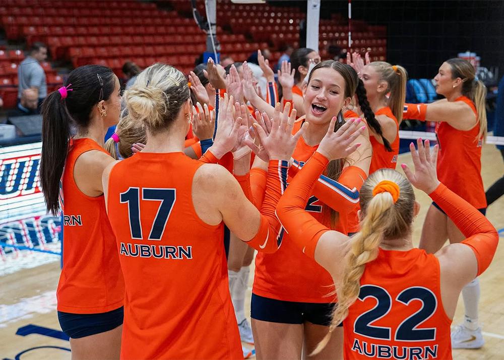 Auburn volleyball players in orange jerseys celebrate together with high fives during a match, with players wearing Nos. 17 and 22 in the foreground and the court and stands in the background.