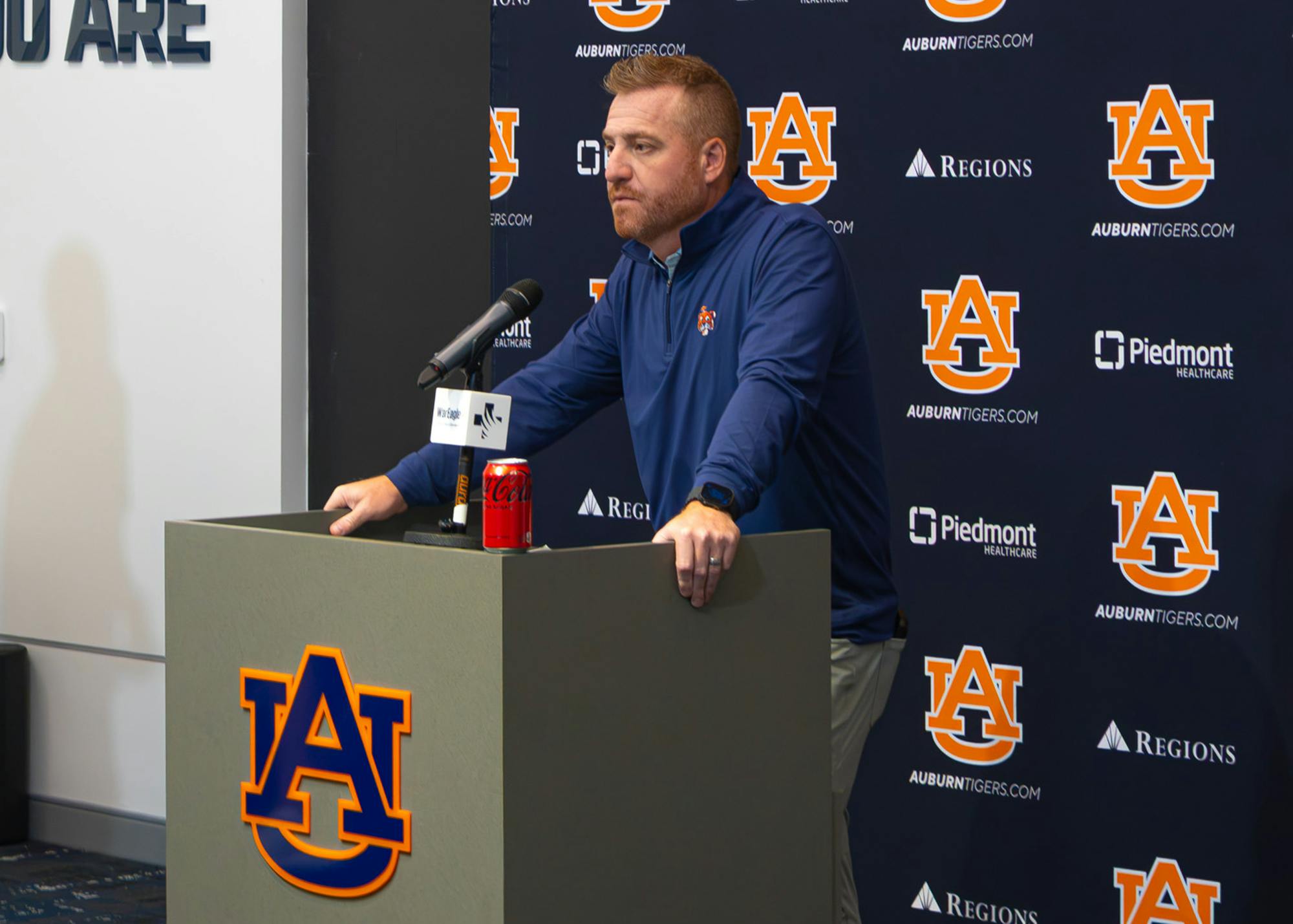 Auburn head coach Alex Golesh speaks at a press conference from a podium in front of an Auburn backdrop.