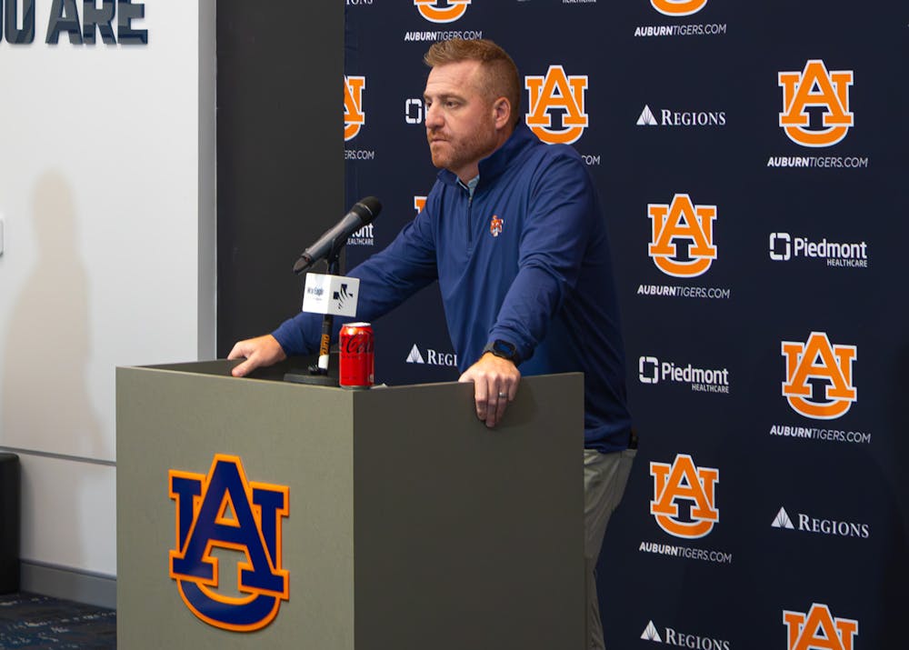 Auburn head coach Alex Golesh speaks at a press conference from a podium in front of an Auburn backdrop.