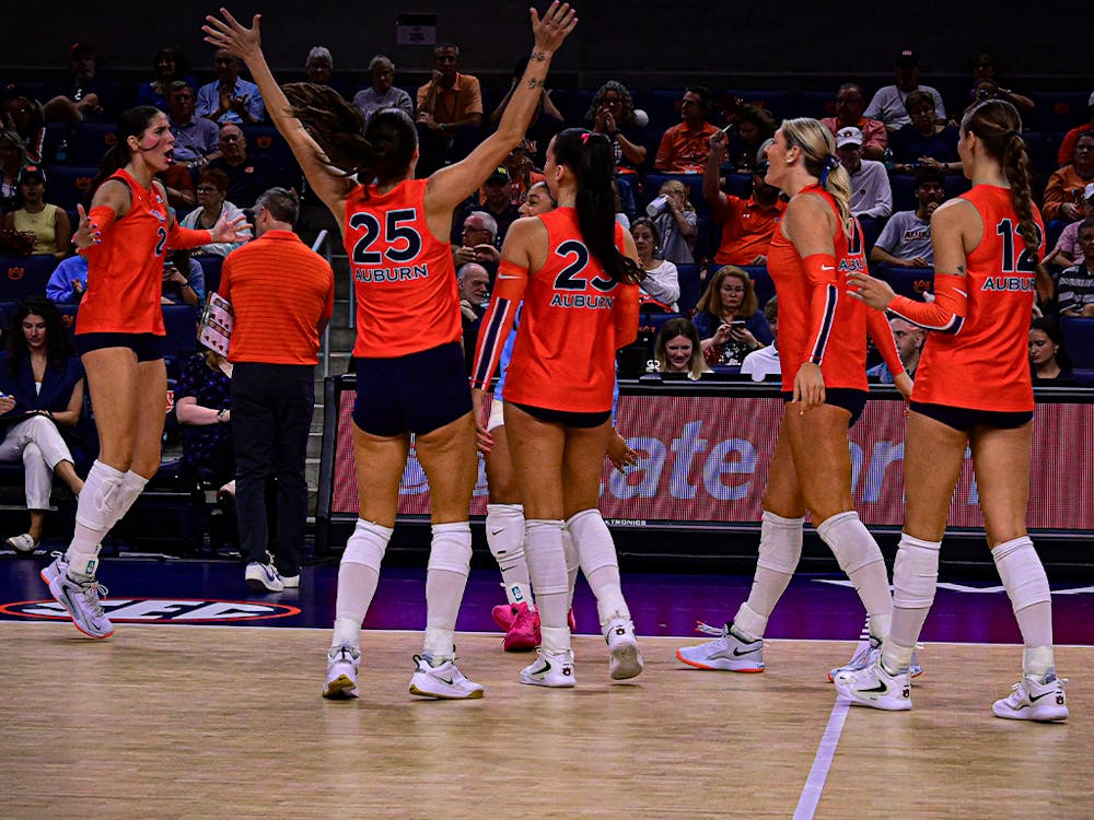 Auburn volleyball players in orange jerseys celebrate a point during a home match as fans cheer in the background.