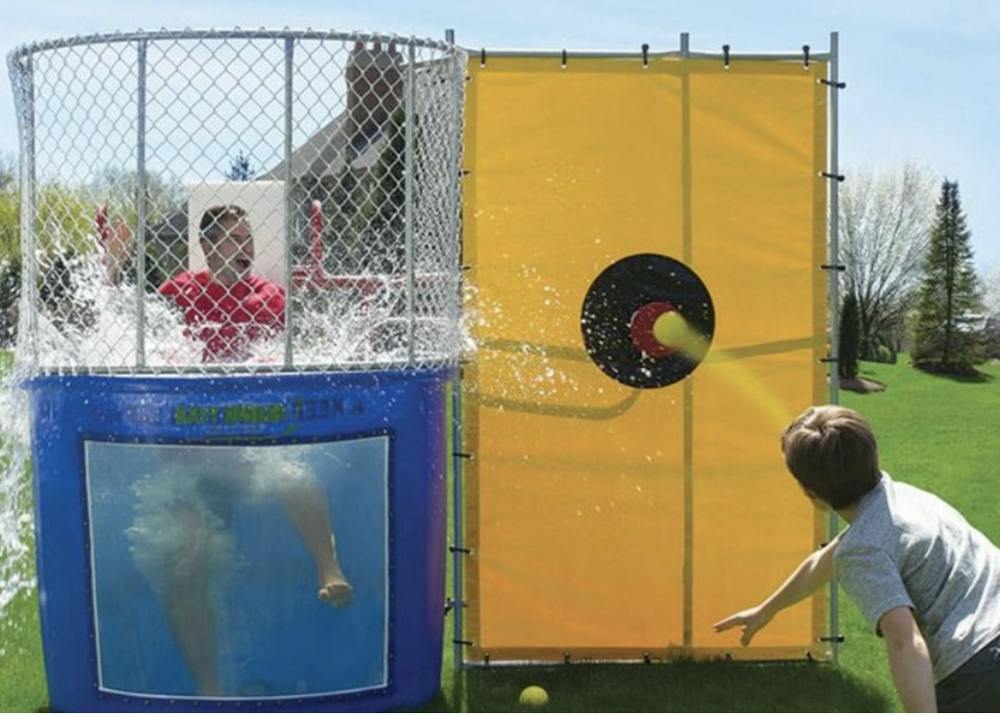 A participant throws a ball at a dunk tank target as water splashes around a person in a red shirt during the 2025 Beat Bama Food Drive.