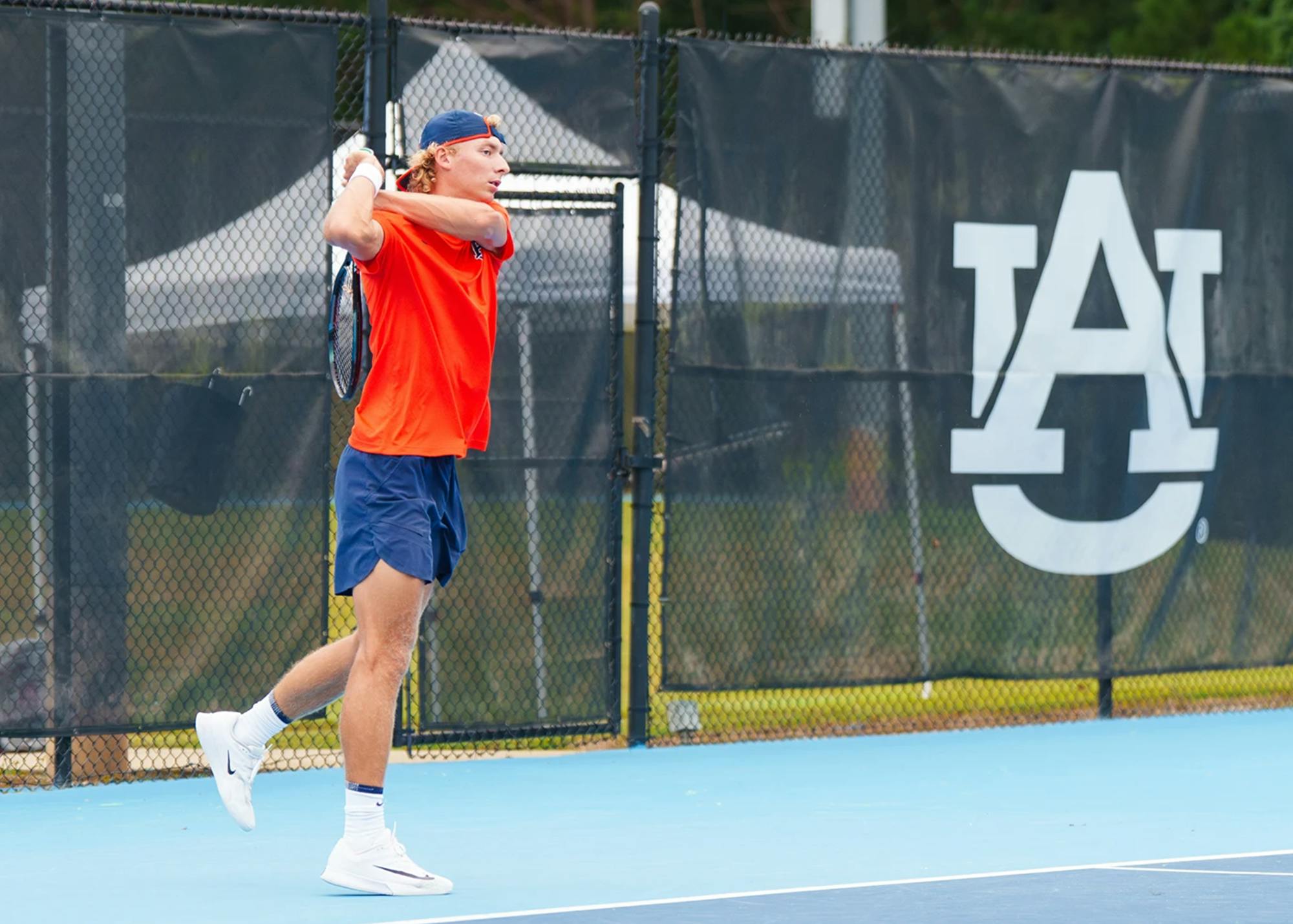 Tyler Bowers, wearing orange, swings a racket on the Auburn tennis court. 