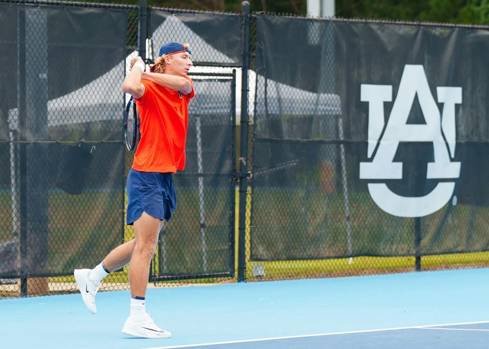 Tyler Bowers, wearing orange, swings a racket on the Auburn tennis court. 