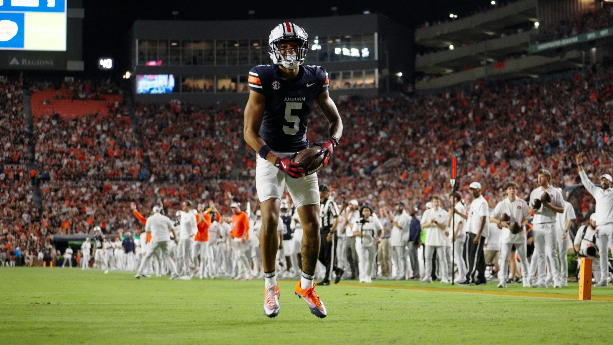 Auburn wide receiver Horatio Fields celebrates in the end zone with the ball in his hands during a night game, as the crowd and sideline cheer in the background.