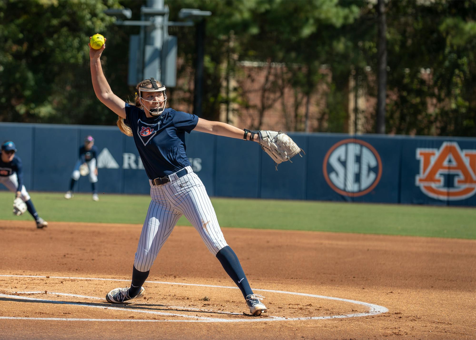 Auburn softball pitcher delivers a pitch during a game, with teammates positioned behind her on the field.