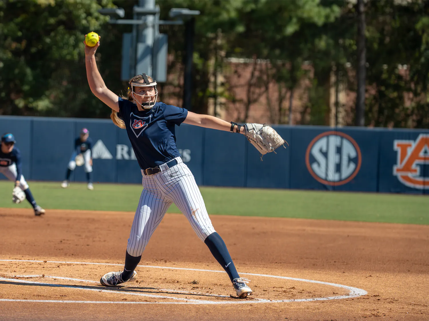 Auburn softball pitcher delivers a pitch during a game, with teammates positioned behind her on the field.