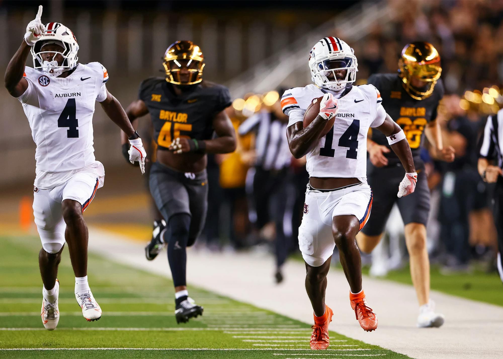 Auburn running back No. 4 runs down the sideline with the ball during a game against Baylor, while teammate No. 14 runs behind him and Baylor defenders give chase.