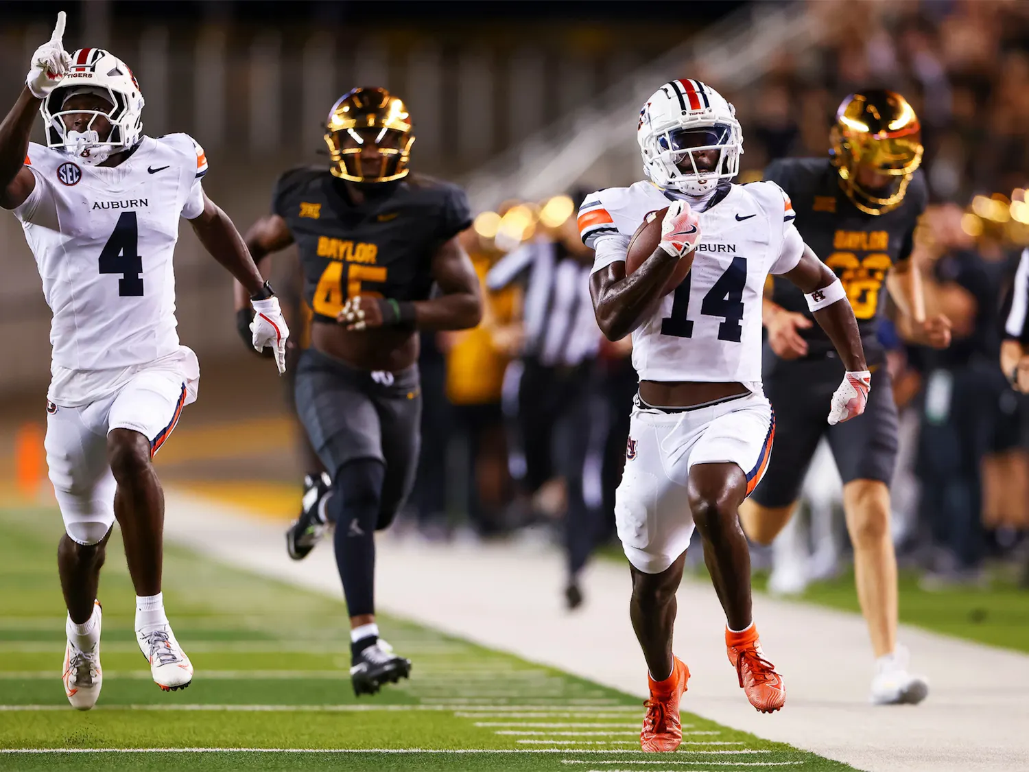 Auburn running back No. 4 runs down the sideline with the ball during a game against Baylor, while teammate No. 14 runs behind him and Baylor defenders give chase.