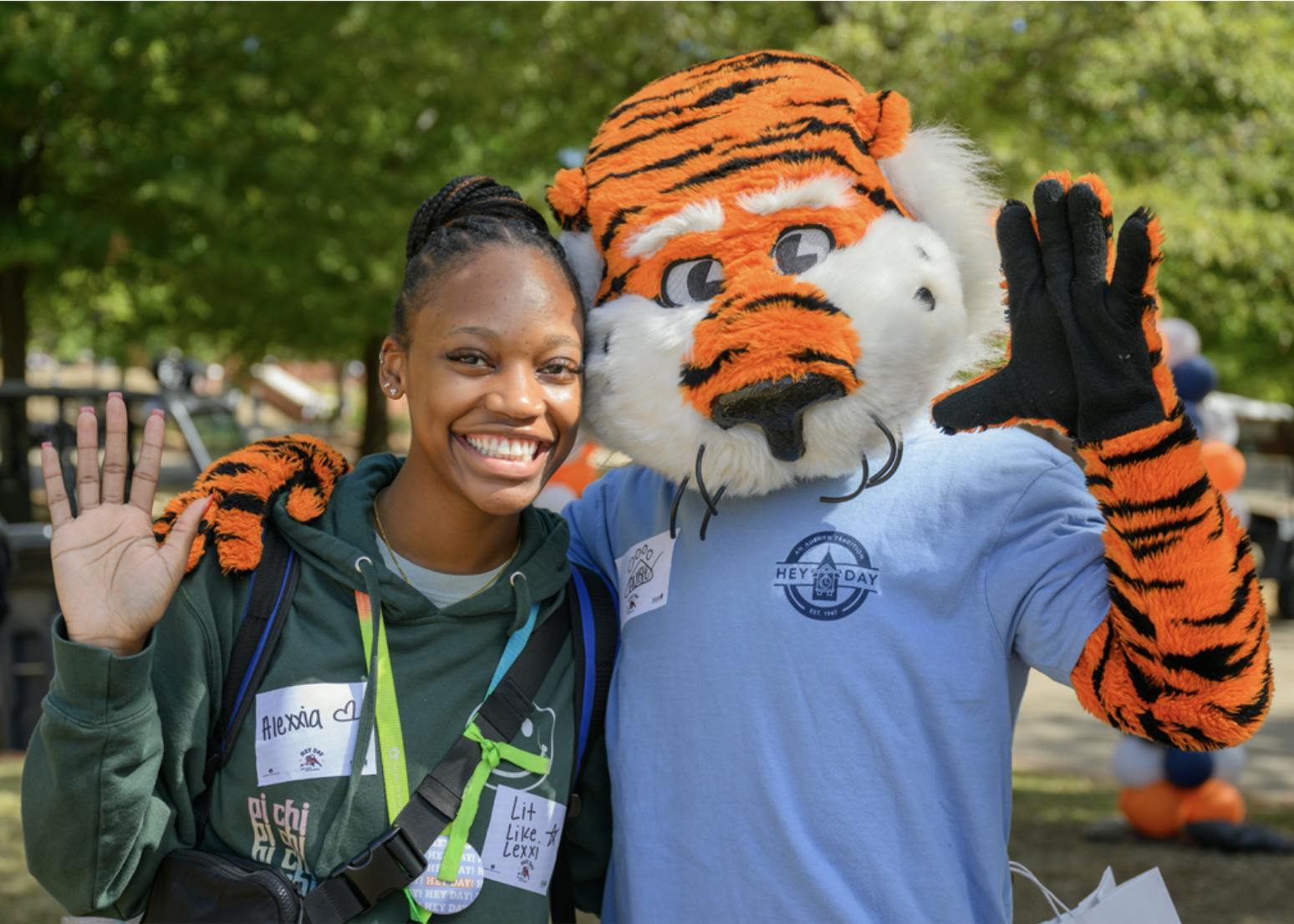 Aubie hugs a smiling woman at Auburn’s Hey Day as they pose for a photo and wave.